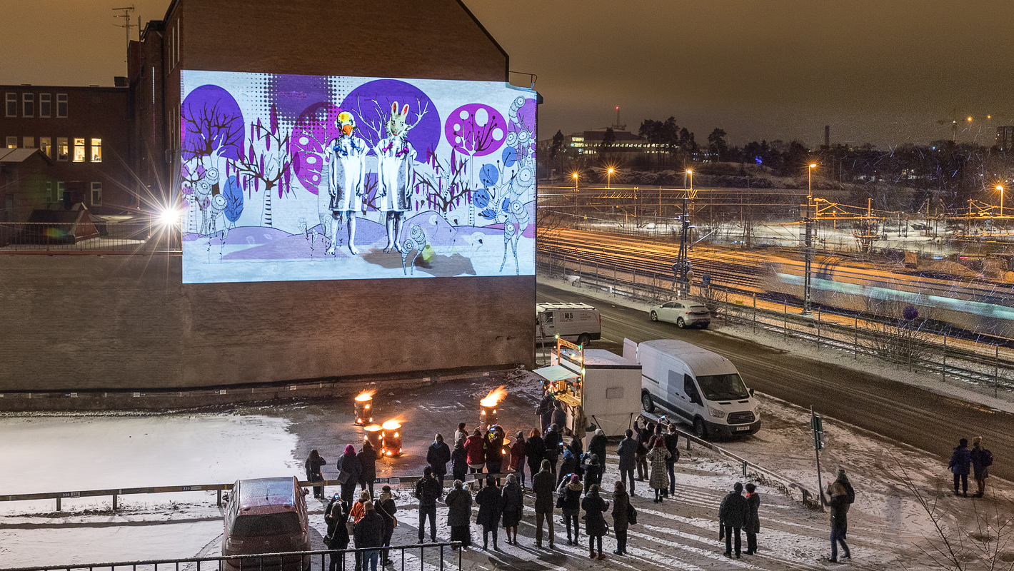 Människor tittar på en projektion på en vägg  i Hagalund. 